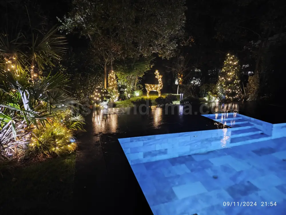 Villa bahçesinde havuz kenarı, ağaçlar ve ışıklı geyik figürüyle yılbaşı LED ışıklandırması, gece